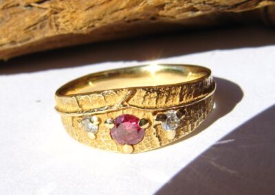 Une alliance Ligne de Vie en or jaune , avec un diamant central rose et deux diamants blancs.