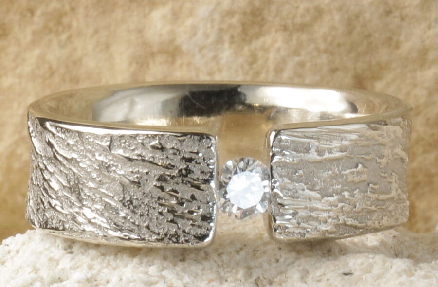 Alliance Silence — Or blanc rhodié — Texture Feu — Un diamant blanc — Atelier du Soleil Fou Alliance Silence avec un diamant central suspendu en largeur 6 mm, bords droits sans bordures, en or blanc rhodié.